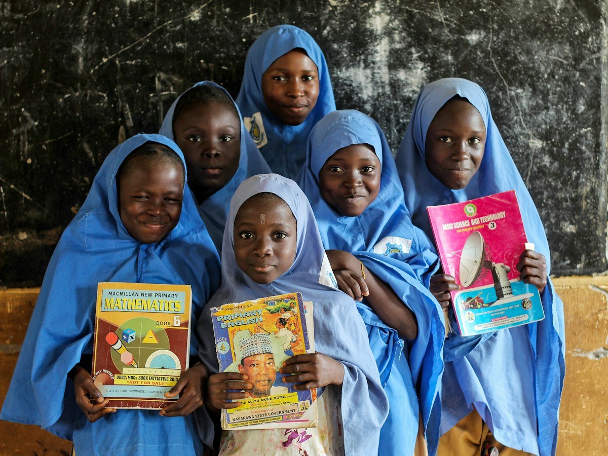 Schoolgirls in blue hijabs proudly holding up their books
