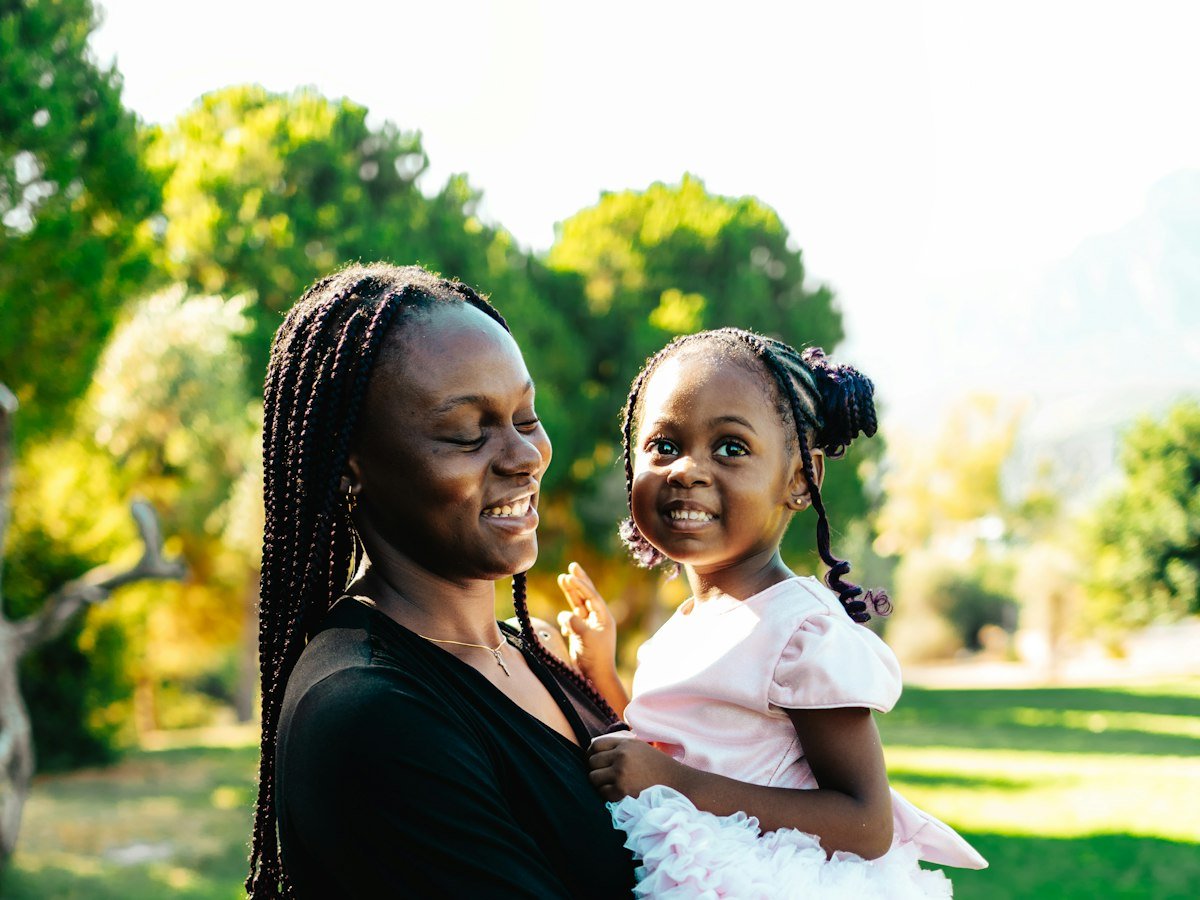A smiling mother holding her young daughter in a park